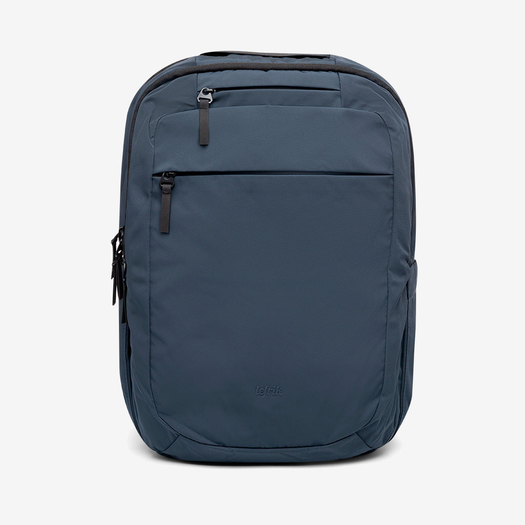 Una mochila azul oscuro con múltiples compartimentos con cremallera, incluido un bolsillo frontal y bolsillos laterales, sobre un fondo blanco liso. El diseño es minimalista y moderno.