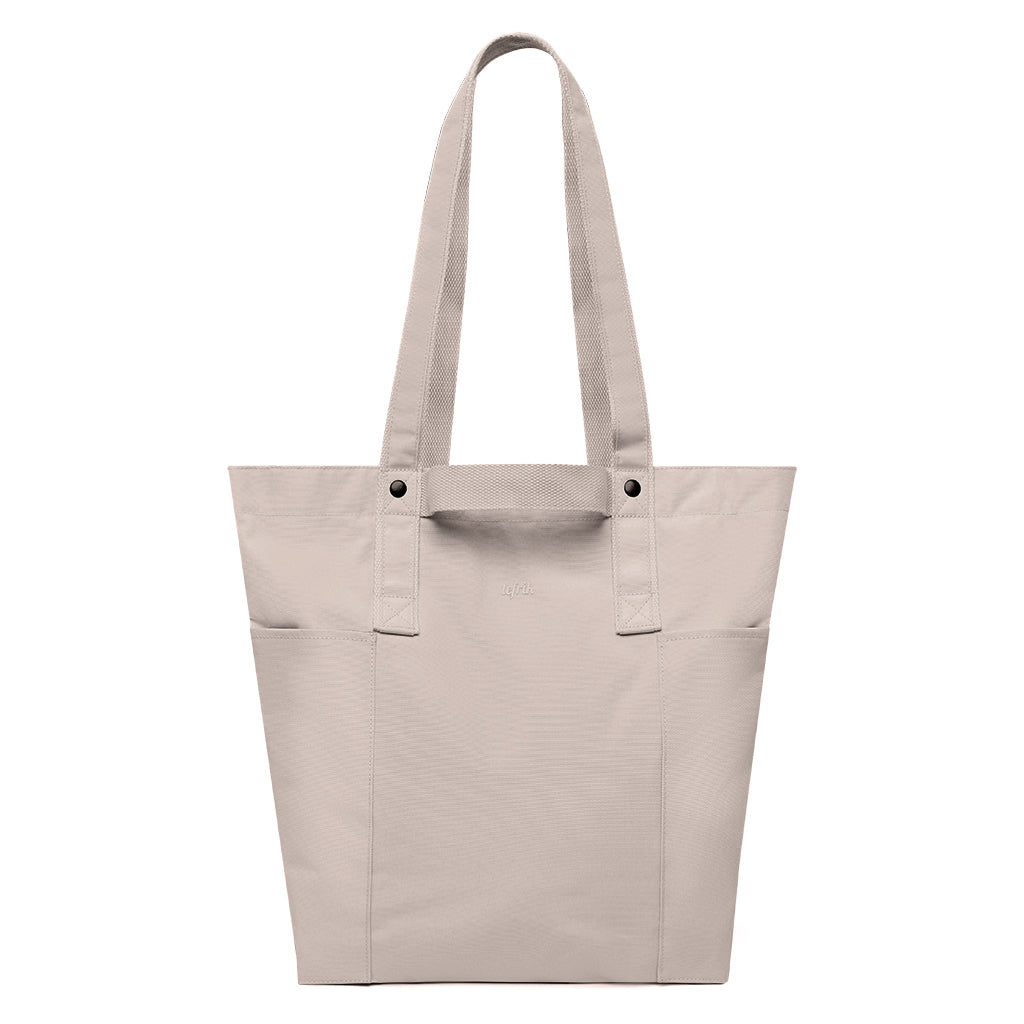 Un bolso tote beige con dos asas largas, diseño minimalista y sin logotipos ni motivos visibles, sobre un fondo blanco liso.